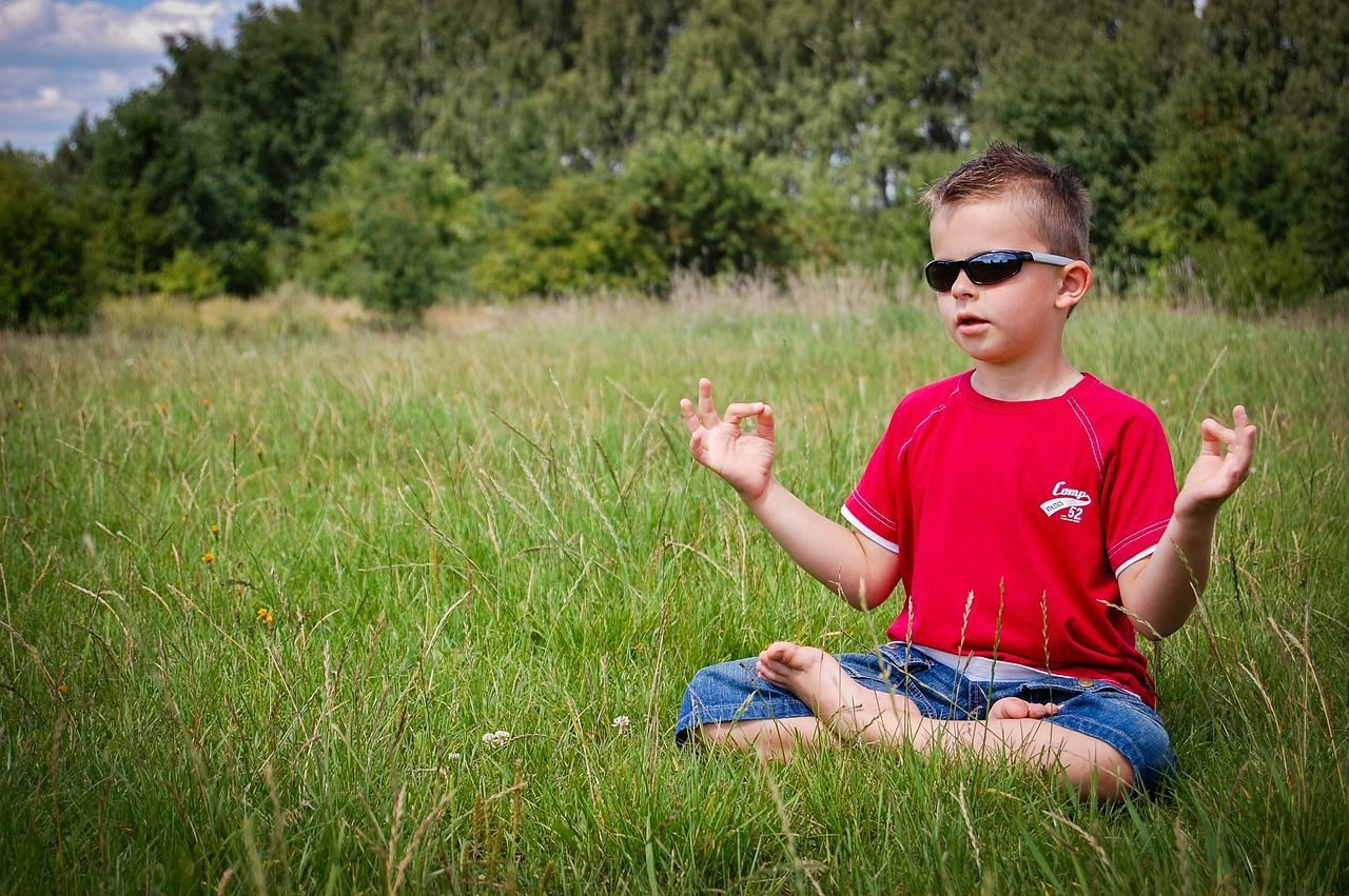 A boy sitting in the grass with his hands raised.